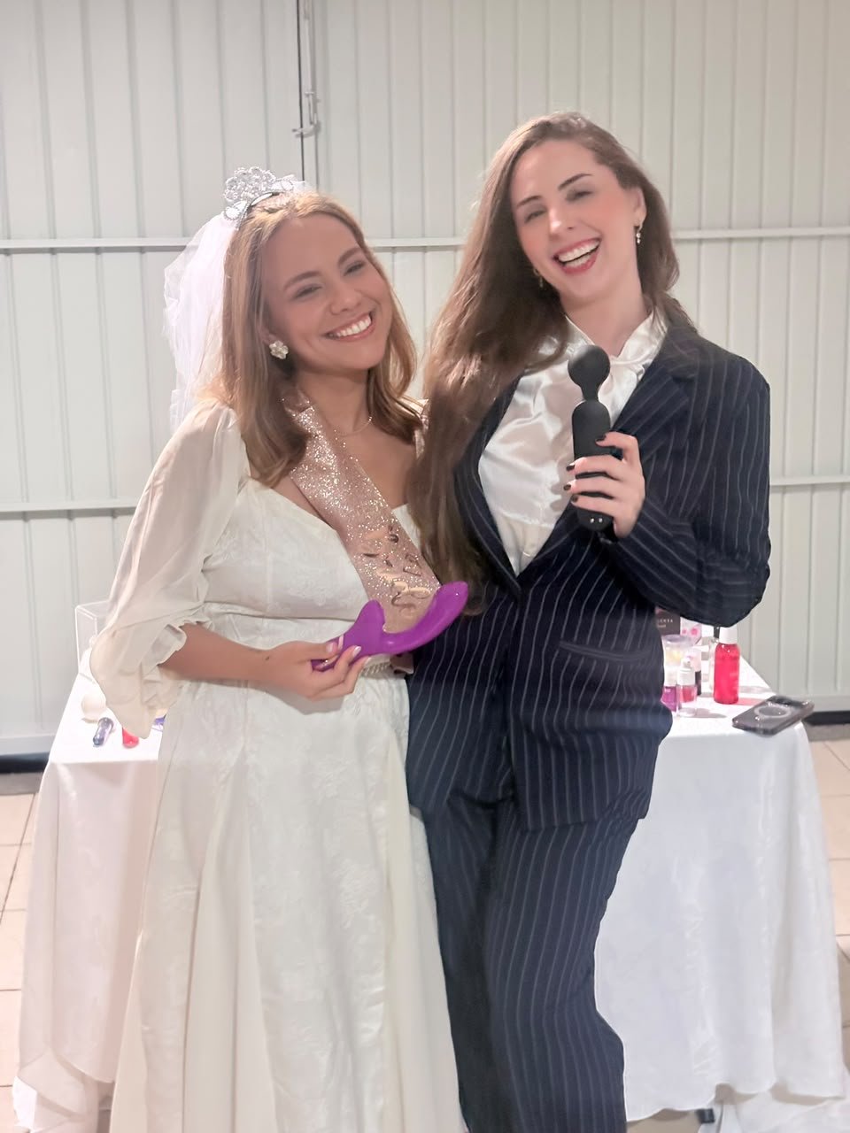 Laura Moraes com a noiva Brendha, as duas segurando produtos, com a vitrine ao fundo